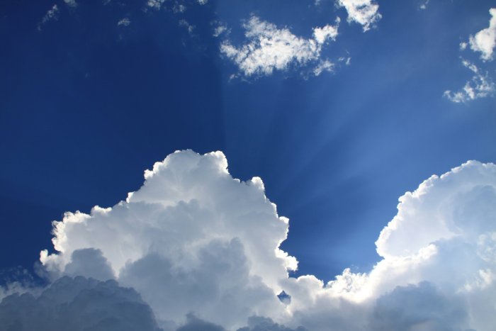Sun rays shining through white clouds in blue sky