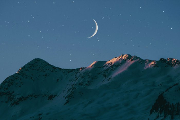 Crescent moon above snow covered mountain peaks