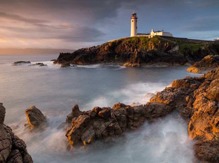 Fanad Head Lighthouse on a rocky coast at sunset