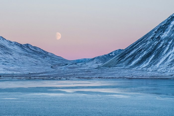 Snowy mountains and frozen lake under a twilight moon