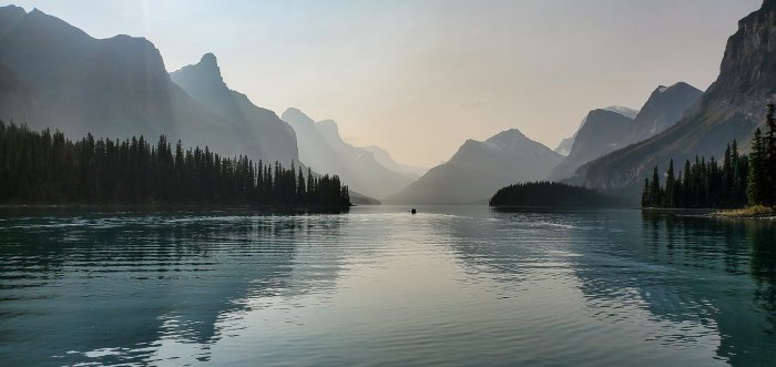 Canoe on a calm lake surrounded by hazy mountains