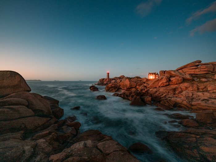 Lighthouse and house on rocky coast at dusk