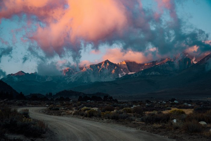 Winding dirt road leading to mountains under sunset clouds