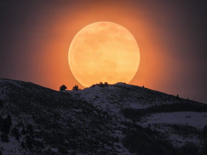 Full moon rising over a snowy mountain ridge