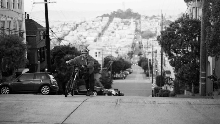Man with bicycle on steep street in The Invite