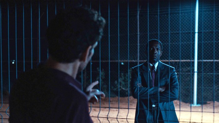 Two men talking through a wire fence in The Fence