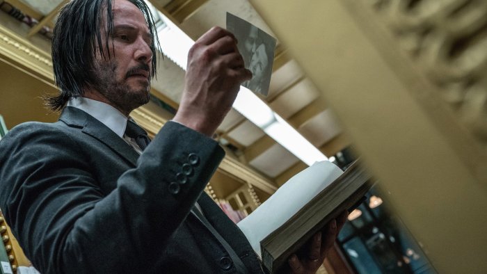 John Wick holding a photograph in a library