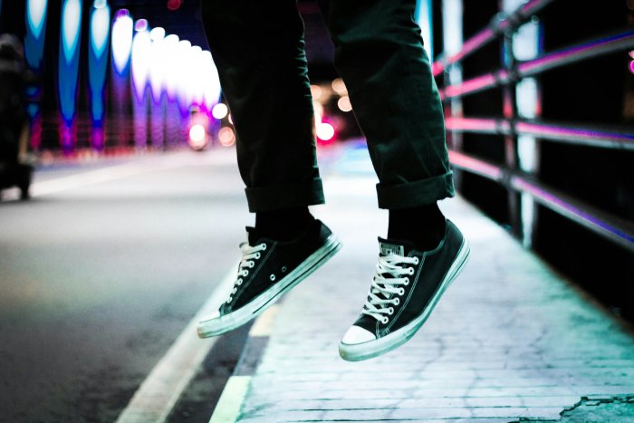 Person jumping in black sneakers on a city bridge