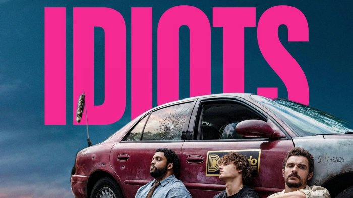 Three men leaning against a damaged car in Idiots