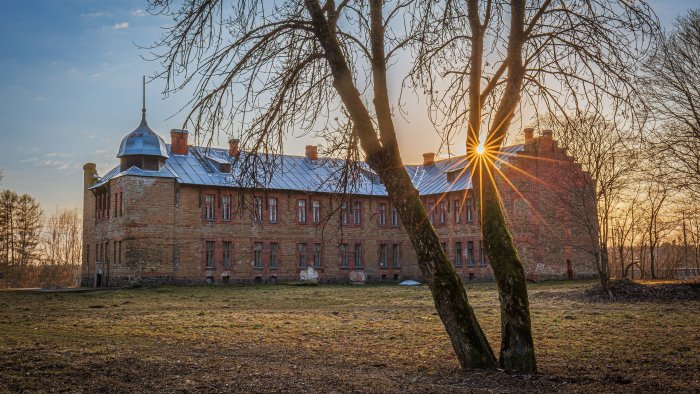 Old brick building at sunset with sunburst through trees