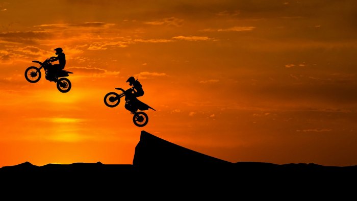 Silhouetted Motocross Riders Jumping at Sunset