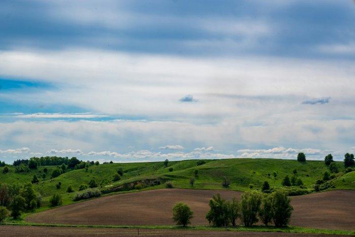 Rolling green hills and plowed fields under cloudy sky