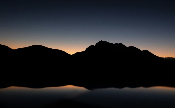 Silhouette of mountains reflected in water at dawn