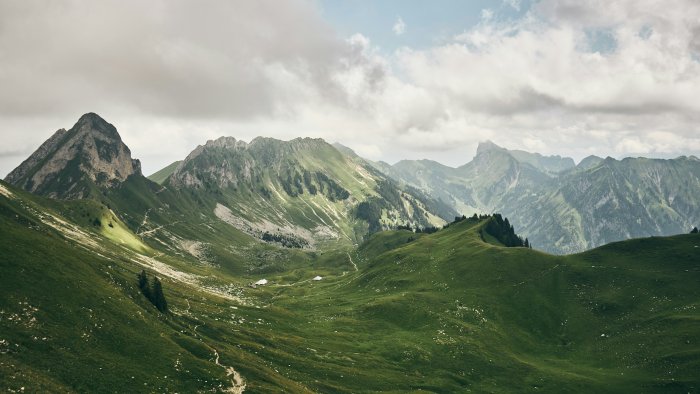 Green hills and rocky mountains under cloudy sky