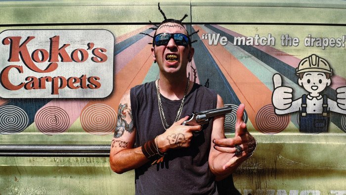 Man with revolver in front of Koko's Carpets van