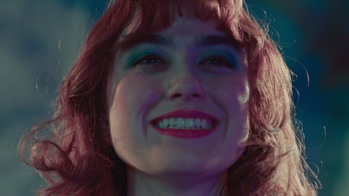 Woman with red hair and blue eyeshadow smiling