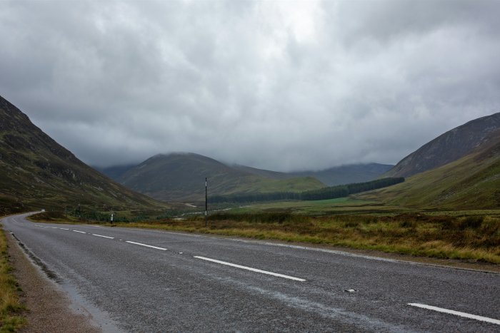 Empty road through Scottish mountains under cloudy sky