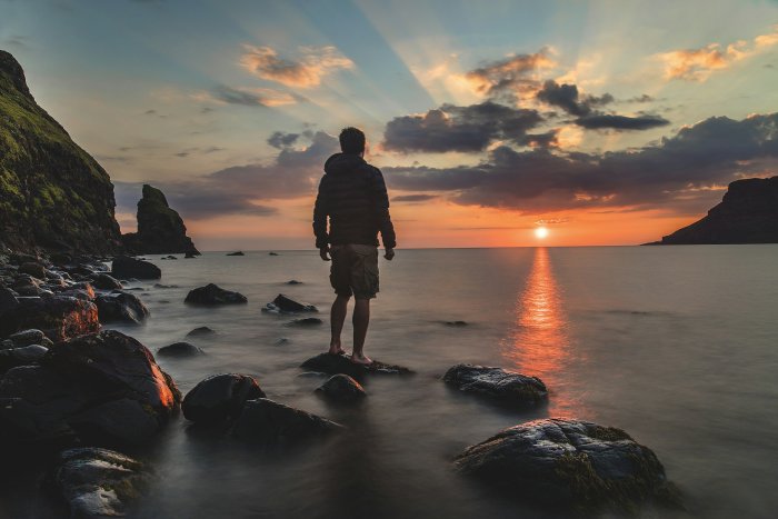 Man watching sunset over the ocean from rocky shore