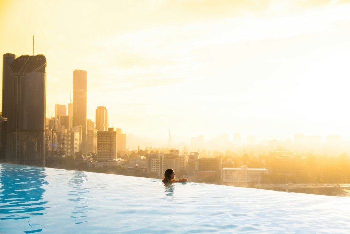 Woman in infinity pool overlooking city at sunset