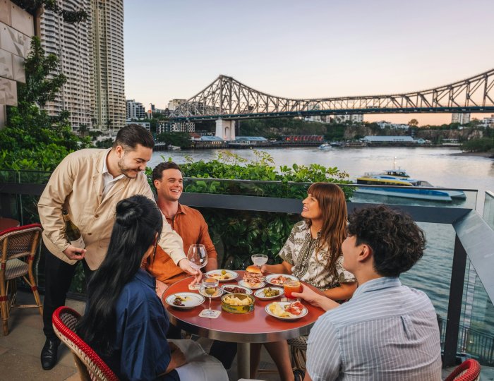 People dining on a terrace overlooking a river and bridge