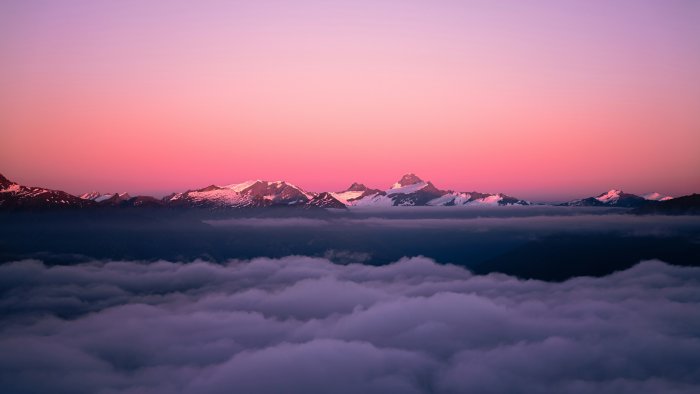 Snow-capped mountains above clouds at sunset