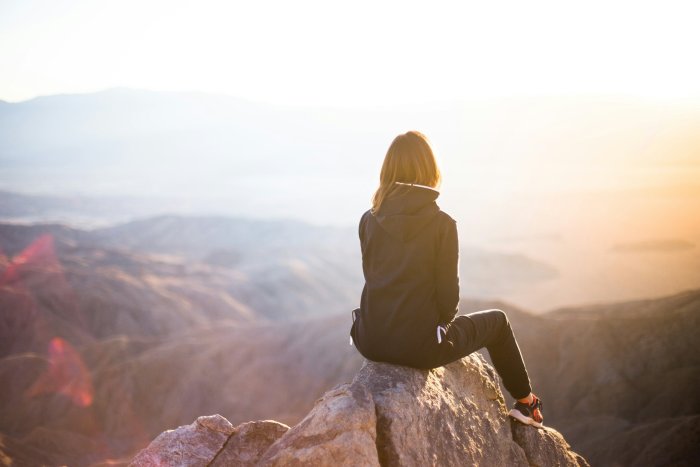 Woman sitting on a rock overlooking a mountain landscape at sunset