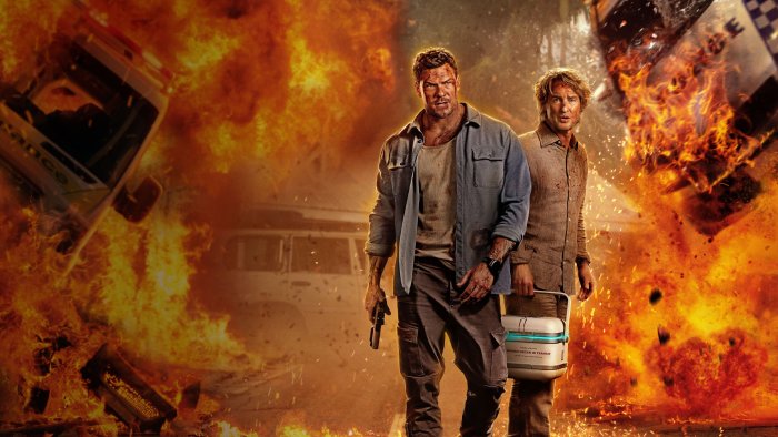 Two men in front of explosions with a medical transport cooler