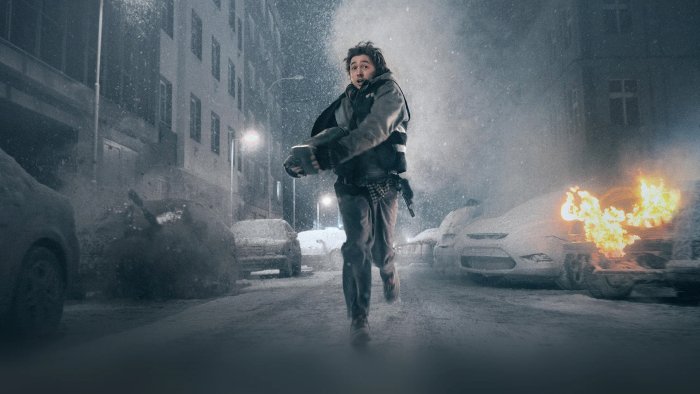 Man running in a snowy city with burning cars