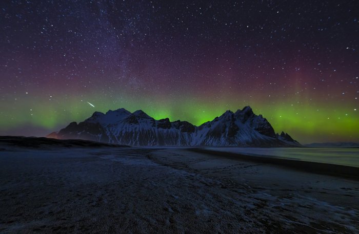 Aurora Borealis over snow-capped mountains and starry sky