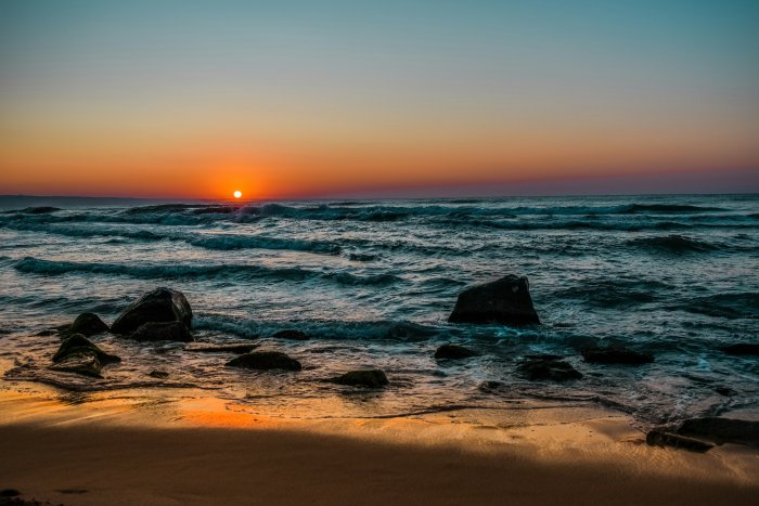 Sunset over ocean waves with rocks on the beach
