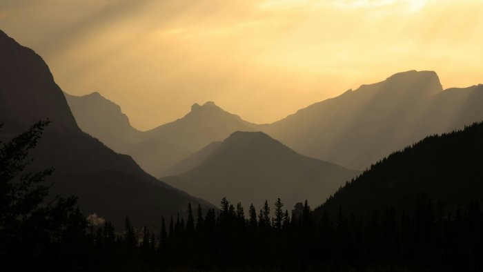 Layered mountain silhouettes at sunset with sunbeams