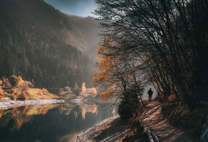 Man walks on a path by a lake in autumn