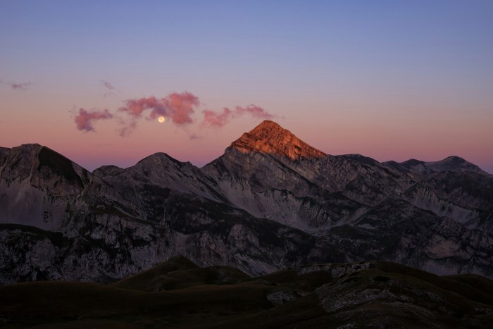 Moonlit mountain peak at sunrise with pink clouds