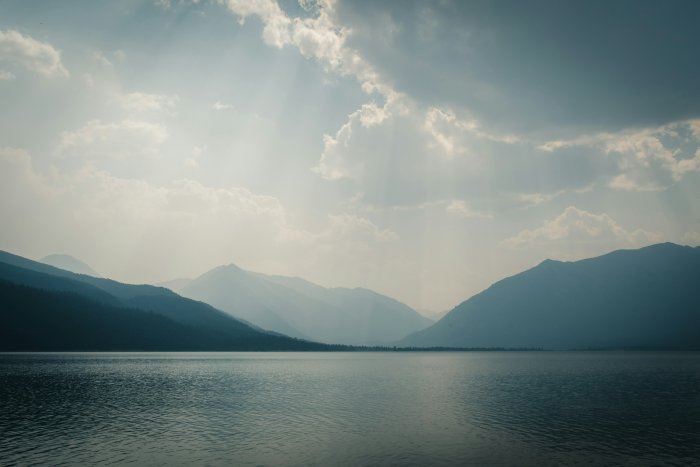 Misty mountains reflected in a calm lake under a cloudy sky
