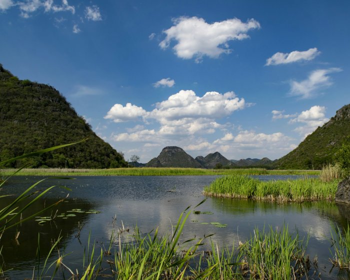 Lush green hills surround a tranquil lake under a blue sky.
