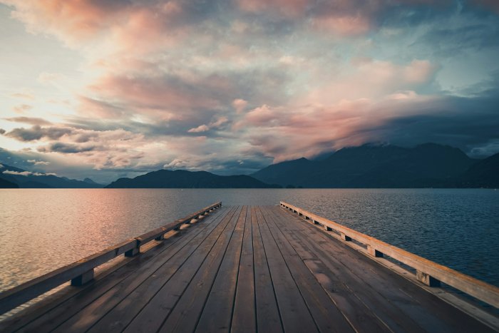 Wooden dock on a lake with mountains and clouds