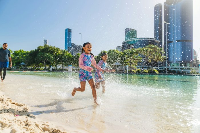 Two girls running through water with a city skyline