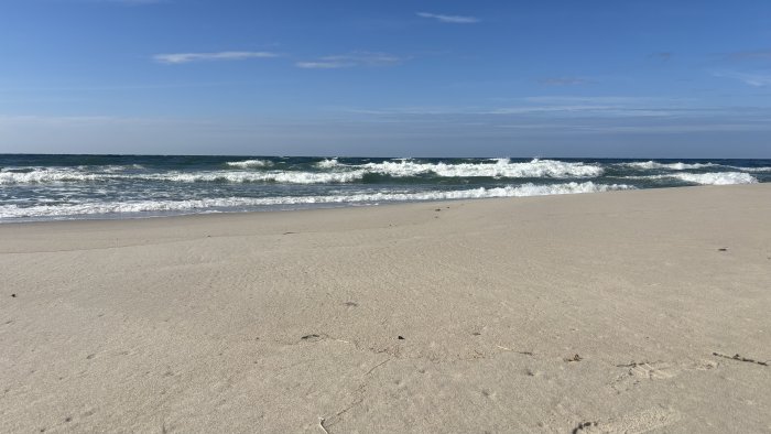 Sandy beach with waves under a blue sky