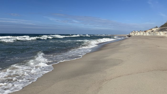Waves crashing on a sandy beach with concrete barriers