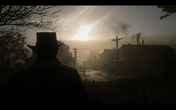 Man in hat looks over dusty town at sunrise