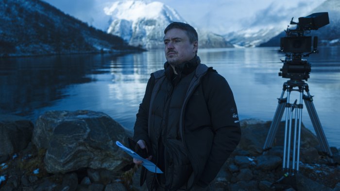 Filmmaker with camera by a fjord