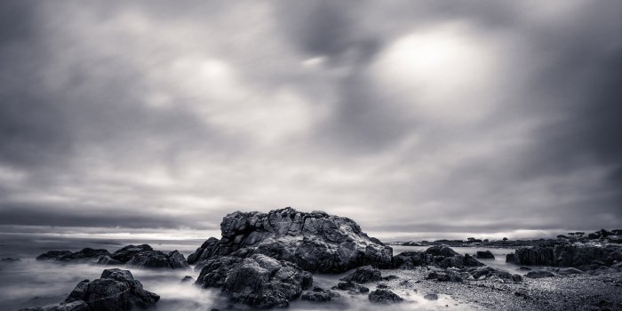 Monochromatic rocky coastline with misty ocean and dramatic clouds