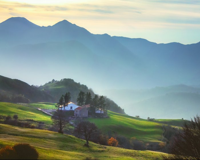 Farmhouse nestled in rolling green hills with mountains