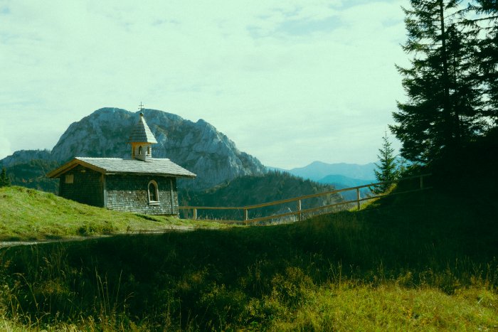 Small chapel on a grassy hill with mountains