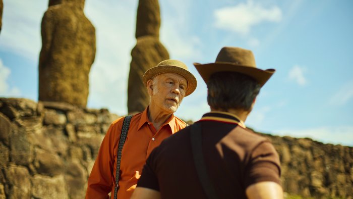 John Malkovich and another man talking near Moai statues