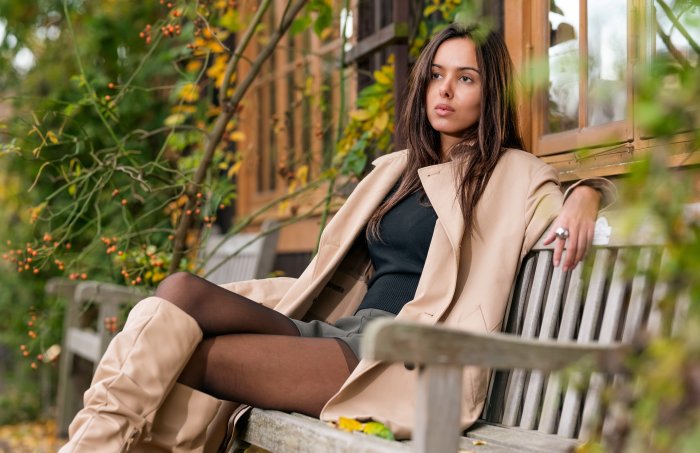 Woman in trench coat sitting on a bench outdoors