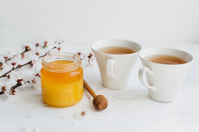 Jar of honey and cups of tea with blossoms