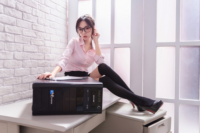 Woman with glasses and thigh-highs sitting by a computer