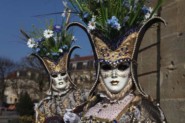 Two people in Venetian carnival costumes with masks and floral headdresses