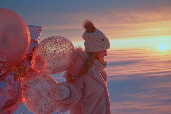 Girl with balloons in winter sunset